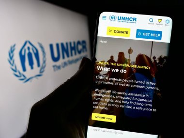 Stuttgart, Almanya - 11-02-2023: Birleşmiş Milletler Mülteciler Yüksek Komiserliği (UNHCR) internet sitesi logosu önünde cep telefonu tutan kişi. Telefon ekranının merkezine odaklan.