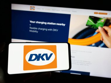 Stuttgart, Almanya - 11-02-2023: Alman B2B ödeme şirketi DKV Mobility 'nin logosuna sahip cep telefonu sahibi kişi iş sayfası önünde. Telefon ekranına odaklan.