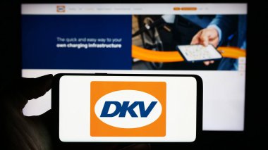 Stuttgart, Almanya - 11-02-2023: Alman B2B ödeme şirketi DKV Mobility 'nin logosuna sahip cep telefonu sahibi kişi iş sayfası önünde. Telefon ekranına odaklan.