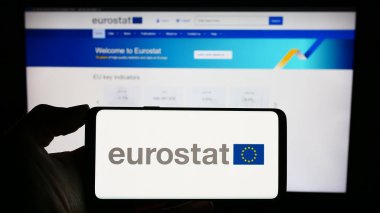 Stuttgart, Almanya - 11-02-2023: AB kurumunun Avrupa İstatistik Bürosu Eurostat logosuna sahip cep telefonu sahibi kişi iş sayfası önünde. Telefon ekranına odaklan.