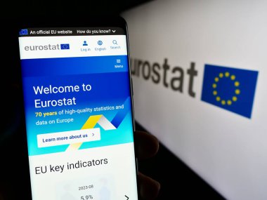 Stuttgart, Almanya - 11-02-2023: AB kurumunun Avrupa İstatistik Bürosu Eurostat web sitesinin logosu önünde cep telefonu tutan kişi. Telefon ekranının merkezine odaklan.