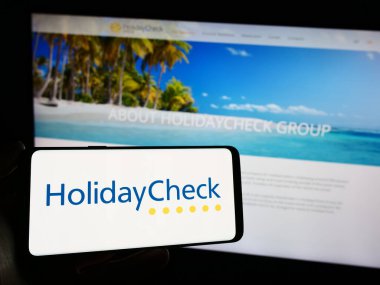 Stuttgart, Almanya - 11-02-2023: İsviçreli seyahat portalı şirketi HolidayCheck AG 'nin logosuyla cep telefonu tutan kişi iş sayfasının önünde. Telefon ekranına odaklan.