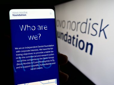 Stuttgart, Almanya - 11-02-2023: Danimarka kuruluşu Novo Nordisk Foundation 'ın internet sayfası ile logo önünde akıllı telefon tutan kişi. Telefon ekranının merkezine odaklan.