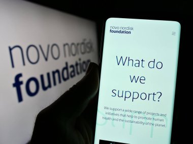 Stuttgart, Almanya - 11-02-2023: Danimarka Novo Nordisk Foundation 'ın logo önündeki web sayfası ile cep telefonu tutan kişi. Telefon ekranının merkezine odaklan.