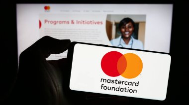 Stuttgart, Almanya - 11-02-2023: Kanada hayır kurumu Mastercard Foundation 'ın logosunun bulunduğu cep telefonu sahibi kişi web sayfası önünde. Telefon ekranına odaklan.