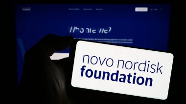 Stuttgart, Almanya - 11-02-2023: İnternet sayfası önünde Danimarkalı Novo Nordisk Foundation logosu olan cep telefonu sahibi kişi. Telefon ekranına odaklan.