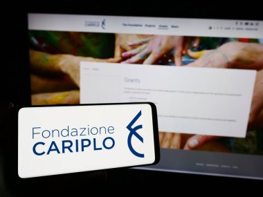 Stuttgart, Almanya - 11-03-2023: İtalyan yardım vakfı Fondazione Cariplo 'nun logosunu web sayfasının önünde tutan kişi. Telefon ekranına odaklan.