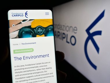 Stuttgart, Almanya - 11-03-2023: İtalyan hayır kurumu Fondazione Cariplo 'nun logo önündeki web sayfası ile akıllı telefon tutan kişi. Telefon ekranının merkezine odaklan.