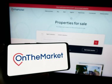 Stuttgart, Almanya - 11-03-2023: İngiliz emlak portalı şirketi TheMarket.com 'un logosuyla cep telefonu sahibi kişi iş sayfasının önünde. Telefon ekranına odaklan.