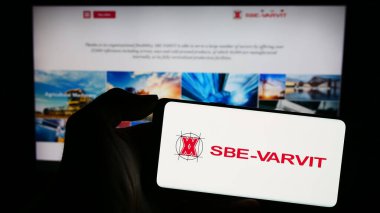 Stuttgart, Germany - 11-03-2023: Person holding mobile phone with logo of Italian mechanical fastening company SBE-VARVIT S.p.A. in front of web page. Focus on phone display. clipart