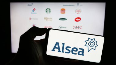 Stuttgart, Germany - 11-03-2023: Person holding mobile phone with logo of Mexican restaurant company Alsea S.A.B. de C.V. in front of business web page. Focus on phone display. clipart