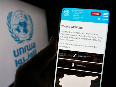 Stuttgart, Almanya - 11-03-2023: Birleşmiş Milletler Plalestine mülteci ajansı UNRWA 'nın internet sayfası ile logo önünde cep telefonu tutan kişi. Telefon ekranının merkezine odaklan.