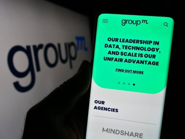 Stuttgart, Almanya - 11-03-2023: İş logosu önünde ABD 'li medya yatırım şirketi GroupM' nin web sayfası ile akıllı telefon tutan kişi. Telefon ekranının merkezine odaklan.