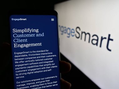 Stuttgart, Almanya - 11-06-2023: ABD 'li yazılım şirketi EngageSmart LLC' nin web sayfası ile akıllı telefon sahibi kişi iş logosu önünde. Telefon ekranının merkezine odaklan.