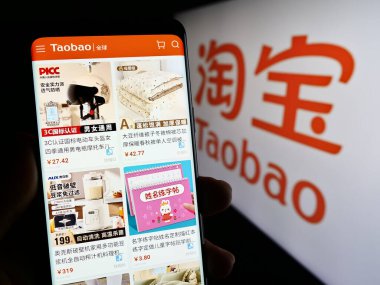 Stuttgart, Almanya - 11-06-2023: Logo önünde Çince çevrimiçi Taobao (Alibaba Group) web sitesi ile akıllı telefon tutan kişi. Telefon ekranının merkezine odaklan.