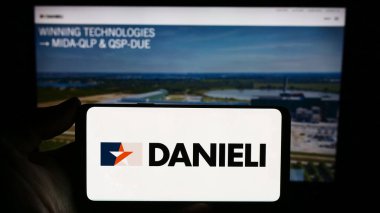 Stuttgart, Almanya - 11-06-2023: İtalyan Danieli C. Officine Meccaniche S.p.A. şirketinin logosunu elinde tutan kişi. Telefon ekranına odaklan.