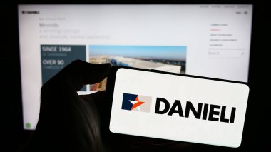 Stuttgart, Almanya - 11-06-2023: İtalyan Danieli C. Officine Meccaniche S.p.A. şirketinin logosuyla cep telefonu tutan kişi iş sayfasının önünde. Telefon ekranına odaklan.