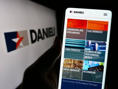 Stuttgart, Almanya - 11-06-2023: İtalyan Danieli C. Officine Meccaniche SpA şirketinin logo önündeki web sayfası ile cep telefonu tutan kişi. Telefon ekranının merkezine odaklan.