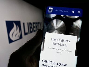 Stuttgart, Germany - 11-06-2023: Person holding cellphone with webpage of British metals company Liberty Steel Group in front of logo. Focus on center of phone display. clipart