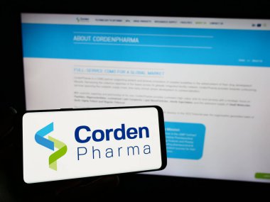 Stuttgart, Germany - 11-07-2023: Person holding smartphone with logo of pharmaceutical CDMO company CordenPharma in front of website. Focus on phone display. clipart