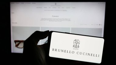 Stuttgart, Almanya - 11-07-2023: İtalyan moda şirketi Brunello Cucinelli S.P.A. 'nın logosuyla cep telefonu tutan kişi iş sayfasının önünde. Telefon ekranına odaklan.