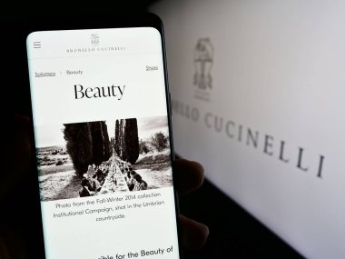 Stuttgart, Almanya - 11-07-2023: İtalyan moda şirketi Brunello Cucinelli S.P.A. 'nın internet sayfası ile logo önünde cep telefonu tutan kişi. Telefon ekranının merkezine odaklan.