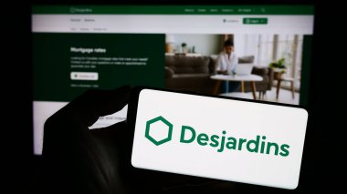 Stuttgart, Almanya - 11-07-2023: Kanadalı finans hizmetleri şirketi Desjardins Group 'un logosunun bulunduğu cep telefonu sahibi kişi web sitesinin önünde. Telefon ekranına odaklan.