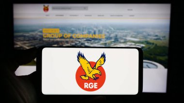 Stuttgart, Almanya - 11-08-2023: Singapur 'lu Royal Golden Eagle (RGE) şirketinin logosunun bulunduğu cep telefonu sahibi kişi iş sayfası önünde. Telefon ekranına odaklan.