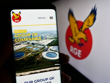 Stuttgart, Almanya - 11-08-2023: Singapur şirketi Royal Golden Eagle 'ın (RGE) logo önünde cep telefonu tutan kişi. Telefon ekranının merkezine odaklan.