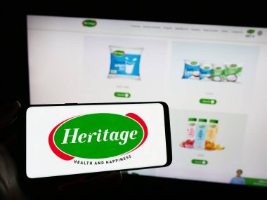 Stuttgart, Almanya - 11-08-2023: Hint süt ürünleri şirketi Heritage Foods Limited 'in logosunun bulunduğu cep telefonu sahibi kişi iş sayfasının önünde. Telefon ekranına odaklan.