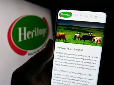 Stuttgart, Almanya - 11-08-2023: Hindistan Süt Ürünleri Şirketi Heritage Foods Limited 'in logosu önünde web sayfası bulunan kişi. Telefon ekranının merkezine odaklan.