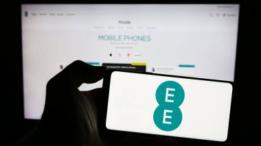 Stuttgart, Almanya - 11-08-2023: İngiliz telekomünikasyon şirketi EE Limited 'in logosuna sahip cep telefonu sahibi kişi iş sayfasının önünde. Telefon ekranına odaklan.