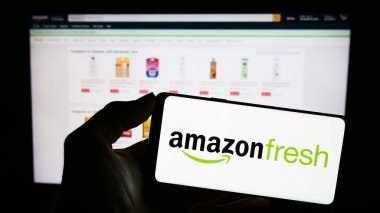 Stuttgart, Almanya - 11-09-2023: Üzerinde Amerikan market perakende şirketi Amazon Fresh 'in logosu bulunan cep telefonu sahibi kişi iş sayfasının önünde. Telefon ekranına odaklan.