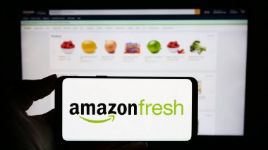 Stuttgart, Almanya - 11-09-2023: Üzerinde ABD 'li market perakende şirketi Amazon Fresh' in logosu olan cep telefonu bulunan kişi iş sayfasının önünde. Telefon ekranına odaklan.