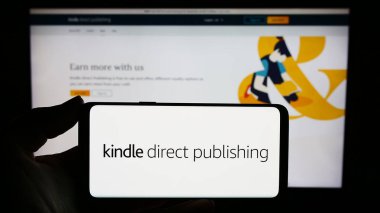 Stuttgart, Almanya - 11-09-2023: İnternet sitesi önünde elinde Amazon e-kitap platformu Kindle Direct Publishing (KDP) logosu bulunan kişi. Telefon ekranına odaklan.