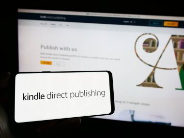 Stuttgart, Almanya - 11-09-2023: Şirketin web sayfası önünde Amazon e-kitap platformu Kindle Direct Publishing 'in (KDP) logosunu elinde tutan kişi. Telefon ekranına odaklan.