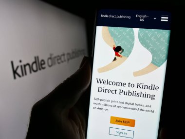 Stuttgart, Almanya - 11-09-2023: Logolu Amazon e-kitap platformu Kindle Direct Publishing (KDP) web sitesi ile cep telefonu tutan kişi. Telefon ekranının merkezine odaklan.