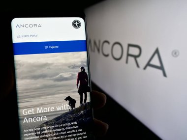 Stuttgart, Almanya - 11-09-2023: ABD 'li yatırım şirketi Ancora Holding Group LLC' nin logo önündeki web sayfası ile cep telefonu tutan kişi. Telefon ekranının merkezine odaklan.