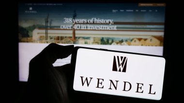 Stuttgart, Almanya - 11-10-2023: Fransız yatırım şirketi Wendel SE 'nin logosuyla cep telefonu tutan kişi iş sayfasının önünde. Telefon ekranına odaklan.