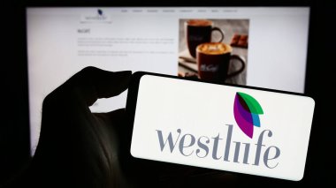 Stuttgart, Almanya - 11-10-2023: Hintli fast food şirketi Westlife Foodworld Limited 'in logosunun bulunduğu cep telefonu sahibi kişi iş sayfasının önünde. Telefon ekranına odaklan.