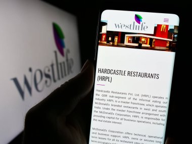 Stuttgart, Almanya - 11-10-2023: Hintli fast food şirketi Westlife Foodworld Limited 'in internet sitesi ile logo önünde cep telefonu tutan kişi. Telefon ekranının merkezine odaklan.