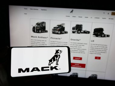 Stuttgart, Almanya - 11-10-2023: Amerikan kamyon üretim şirketi Mack Trucks Inc. 'in logosu olan cep telefonu sahibi kişi web sayfasının önünde. Telefon ekranına odaklan.
