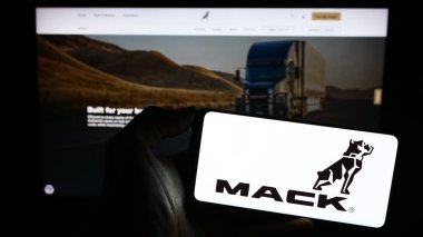 Stuttgart, Almanya - 11-10-2023: ABD 'li kamyon üreticisi Mack Trucks Inc.' in logosu olan cep telefonu sahibi kişi iş sayfasının önünde. Telefon ekranına odaklan.