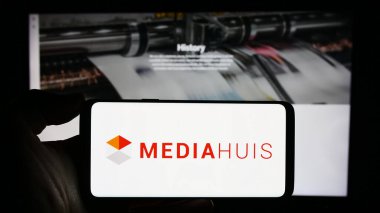 Stuttgart, Almanya - 11-10-2023: Belçikalı medya şirketi Mediahuis N.V. 'nin logosuyla cep telefonu sahibi kişi iş sayfasının önünde. Telefon ekranına odaklan.