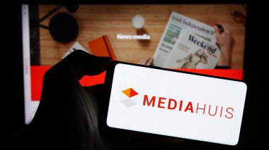 Stuttgart, Almanya - 11-10-2023: Belçikalı medya şirketi Mediahuis N.V. 'nin logosuyla cep telefonu tutan kişi iş sayfasının önünde. Telefon ekranına odaklan.