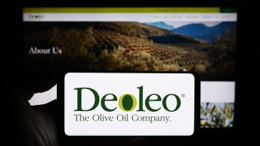 Stuttgart, Almanya - 11-11-2023: Üzerinde İspanyol petrol işleme şirketi Deoleo SA 'nın logosu bulunan cep telefonu sahibi kişi iş sayfasının önünde. Telefon ekranına odaklan.