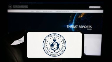 Stuttgart, Germany - 11-11-2023: Person holding smartphone seal logo of United States Defense Intelligence Agency (DIA) in front of website. Focus on phone display. clipart