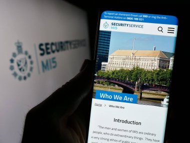 Stuttgart, Germany - 11-11-2023: Person holding cellphone with webpage of British counter-intelligence agency Security Service (MI5) with logo. Focus on center of phone display. clipart