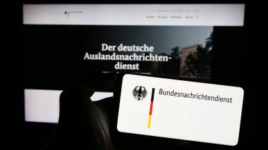 Stuttgart, Germany - 11-11-2023: Person holding mobile phone with logo of German intelligence agency Bundesnachrichtendienst (BND) in front of web page. Focus on phone display. clipart