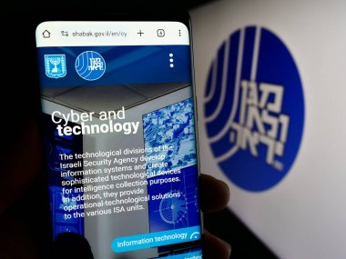 Stuttgart, Almanya - 11-12-2023: İsrail Güvenlik Ajansı 'nın (ISA, Shin Bet) internet sayfası logonun önünde cep telefonu tutan kişi. Telefon ekranının merkezine odaklan.